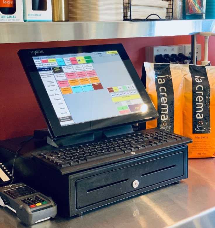 terminal-bancario-en-comercio Terminal bancario en comercio junto a caja registradora y pantalla táctil